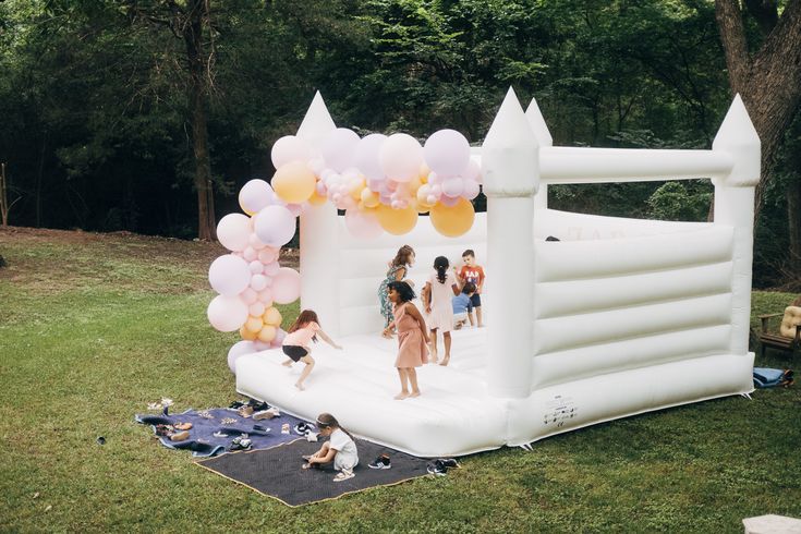 Modern white bounce house with a neutral balloon garland at a Dallas backyard birthday